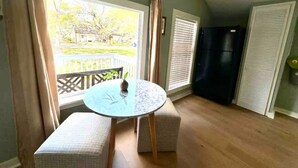 A room with a round table, two cushioned benches, a window with blinds, a black refrigerator, and a door with a louvered design. - Private Coastal Cottage on James Island (Charleston)