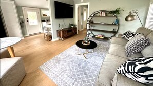 A living room with a round coffee table, a sofa with patterned cushions, a bookshelf, and a flat-screen TV mounted on the wall. - Private Coastal Cottage on James Island (Charleston)
