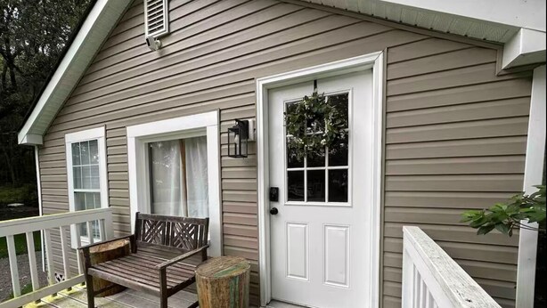 A wooden porch with a bench and a small table, a white door with a window, and a mailbox. - Private Coastal Cottage on James Island (Charleston)