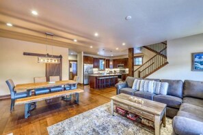A spacious living room with a wooden dining table, a sofa, and a staircase leading to an upper level. - The Alders Townhomes in East Keystone - Luxury 3 Bedroom + Den (Keystone)