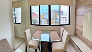 Un comedor moderno con una mesa de vidrio y cuatro sillas, ventanas amplias con vistas a la ciudad y una pared decorativa de madera.