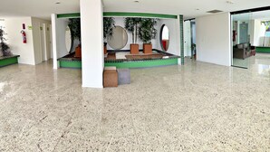 Un vestíbulo espacioso con piso pulido, una zona de estar con un banco y plantas en macetas.