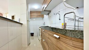 A modern kitchen with white tiles, wooden cabinets, a granite countertop, and a stainless steel sink.