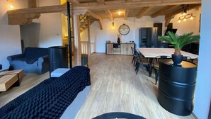 A spacious living area with a wooden ceiling, a dining table with chairs, a sofa, a coffee table, and a potted plant.