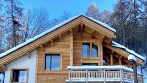 A wooden cabin with a balcony, a garage, and a snow-covered roof.
