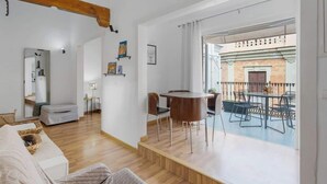 A modern living room with a wooden floor, a sofa, a dining table with chairs, and a balcony with outdoor furniture. - Penthouse in Málaga by Costarentals - MAL01 (Málaga)