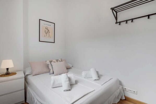 A neatly made bed with white linens and towels, a bedside lamp, and a framed artwork on the wall.