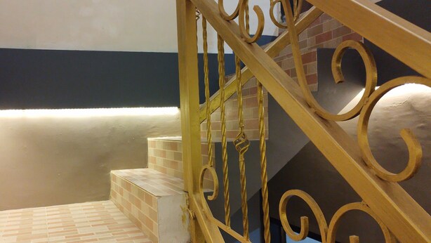 Un escalier avec une rampe en métal jaune et un sol carrelé.