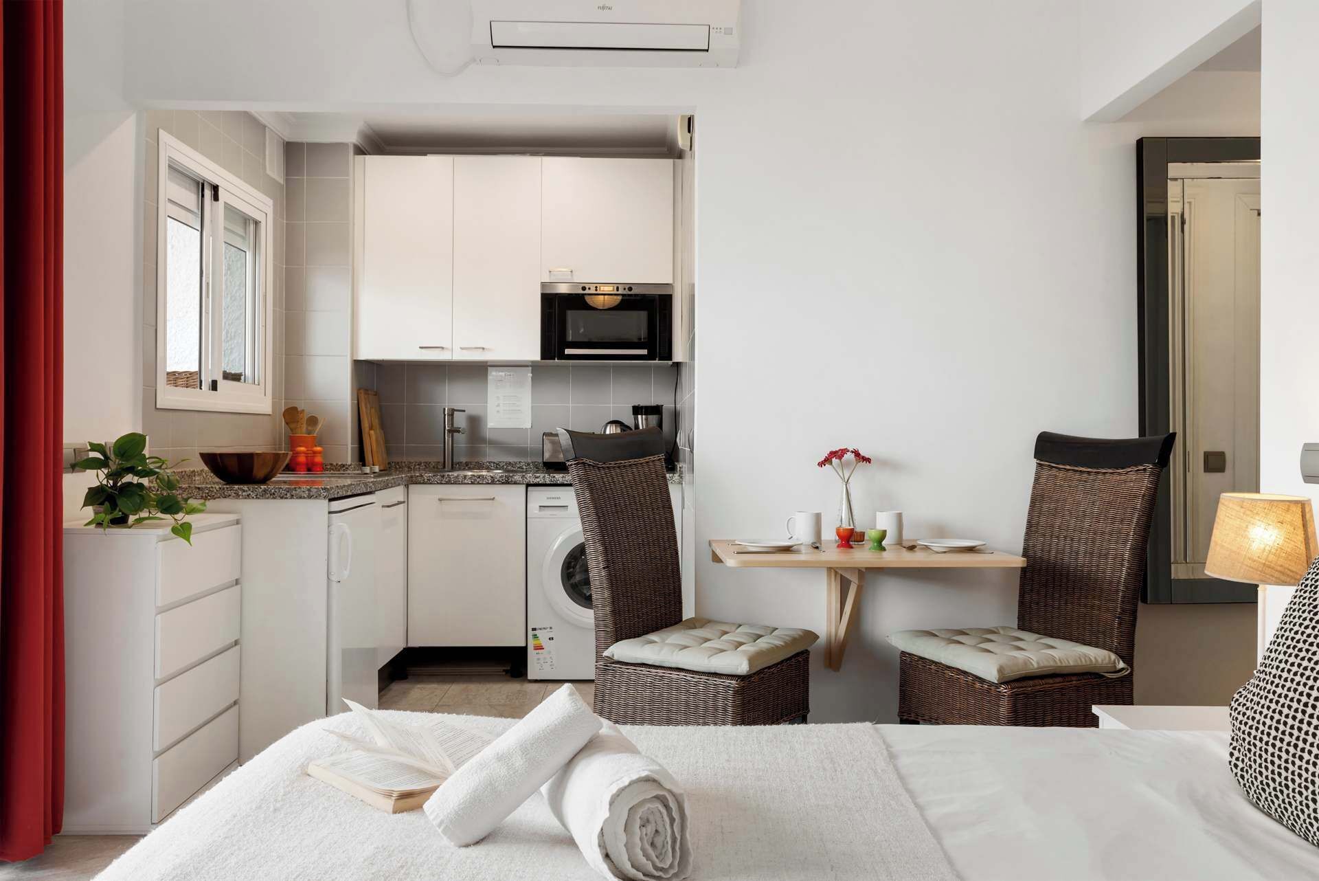 Een kleine hotelkamer met een bed, een eethoekje, een kitchenette en een wasmachine.