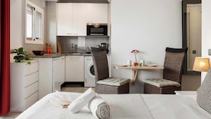 Une chambre d’hôtel compacte comprenant un lit, un petit coin repas, une kitchenette et un lave-linge.