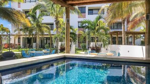 A swimming pool with clear blue water, surrounded by palm trees and blue chairs.