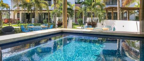 A swimming pool with clear blue water, surrounded by palm trees and blue chairs.