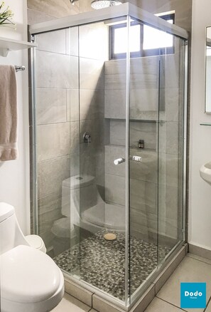 A glass-enclosed shower with a tiled floor, a toilet, and a sink.