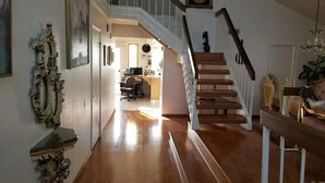 Un hall d’entrée spacieux avec un escalier en bois, un bureau avec un ordinateur et un élément décoratif mural.