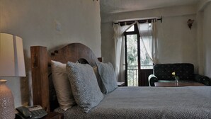 Una camera da letto con un letto, una testata in legno, un comodino con lampada e telefono, una finestra con tende e una sedia con un vaso di fiori.