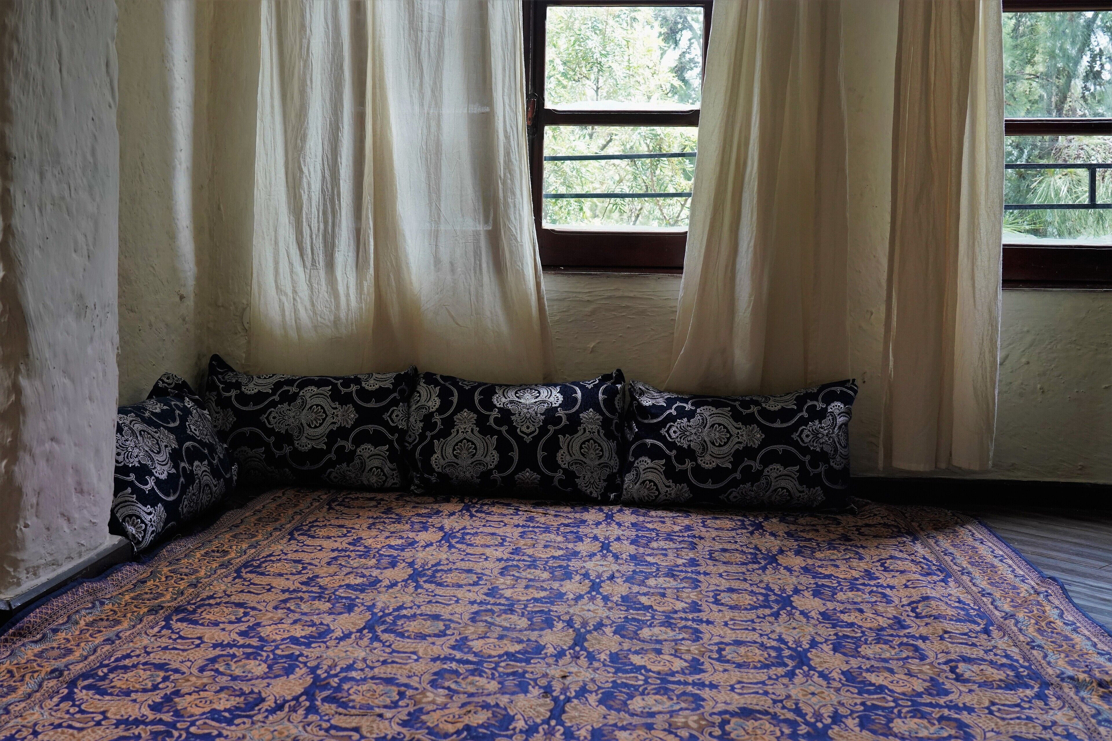 A room with a patterned bedspread, a window with curtains, and a view of greenery outside.