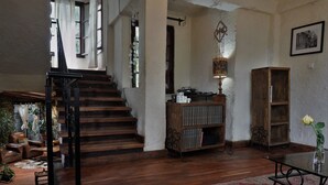Una scala in legno conduce a un piano superiore, con una libreria, un tavolo con un vaso e un tappeto rosso decorato.