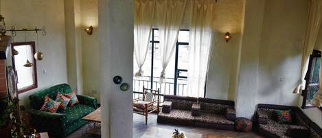 Ein geräumiges Wohnzimmer mit einem grünen Sofa, gemusterten Sofas, einem Holztisch und einem großen Fenster mit Vorhängen.