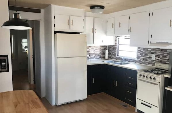 Kitchen features a refrigerator, stove, and sink, with a tiled backsplash and window above the sink.