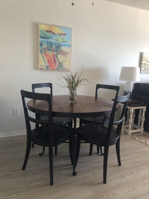 A dining area with a round wooden table, four black chairs, and a potted plant. - THE BEACH IS OPEN ALL YEAR!
Start Planning Your Fall and Winter Vacation Today! (Gulf Shores)