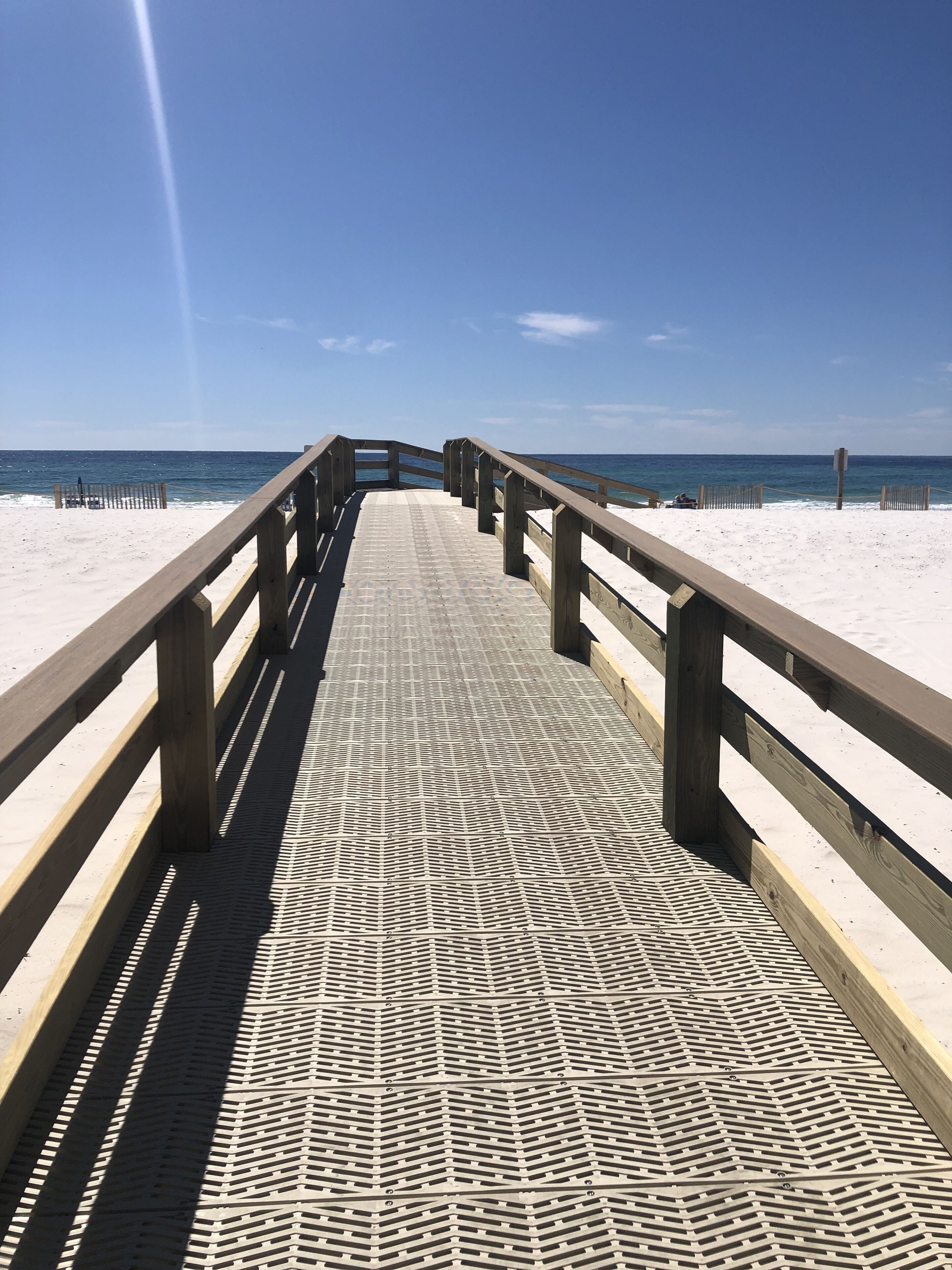 A wooden pier leading to a sandy beach with a clear sky.