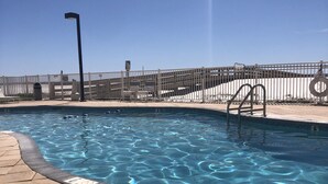Una piscina con acqua cristallina e blu, circondata da un solarium piastrellato e una recinzione.