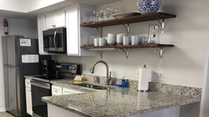 Una cucina moderna con un piano di lavoro in granito, elettrodomestici in acciaio inossidabile, mobili in legno bianco e un'isola con sgabelli da bar.