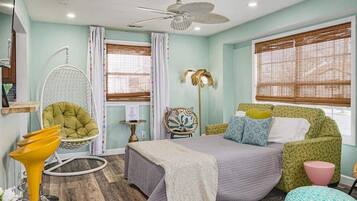 A bedroom with a bed, a chair, a table, and a ceiling fan.