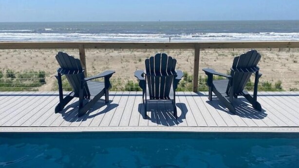 A poolside area with three Adirondack chairs facing a beach. - Thibodeaux's Beach House (Grand Isle)
