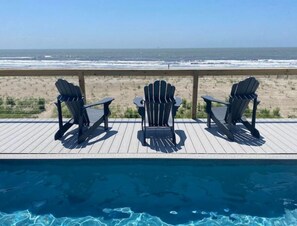Un espace aménagé au bord de la piscine, avec trois fauteuils Adirondack donnant sur une plage.