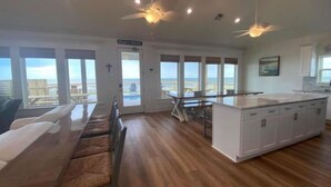 A spacious kitchen with a large island, a dining area with a view, and a ceiling fan. - Thibodeaux's Beach House (Grand Isle)