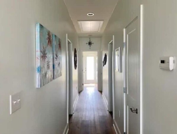 Un couloir doté d’un plancher en bois, de murs blancs et d’un luminaire au plafond. Des portes se trouvent sur le côté droit et une porte se trouve au bout du couloir.