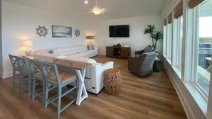 A spacious living area with a wooden dining table, white sofa, and a flat-screen TV mounted on the wall. - Thibodeaux's Beach House (Grand Isle)