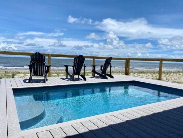 Relax by the oceanfront pool surrounded by Adirondack chairs and a wooden deck.