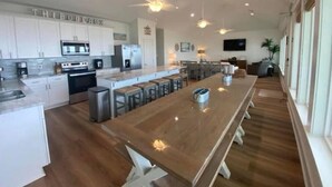 A spacious kitchen with a long island, white cabinets, stainless steel appliances, and a dining area with bar stools. - Thibodeaux's Beach House (Grand Isle)
