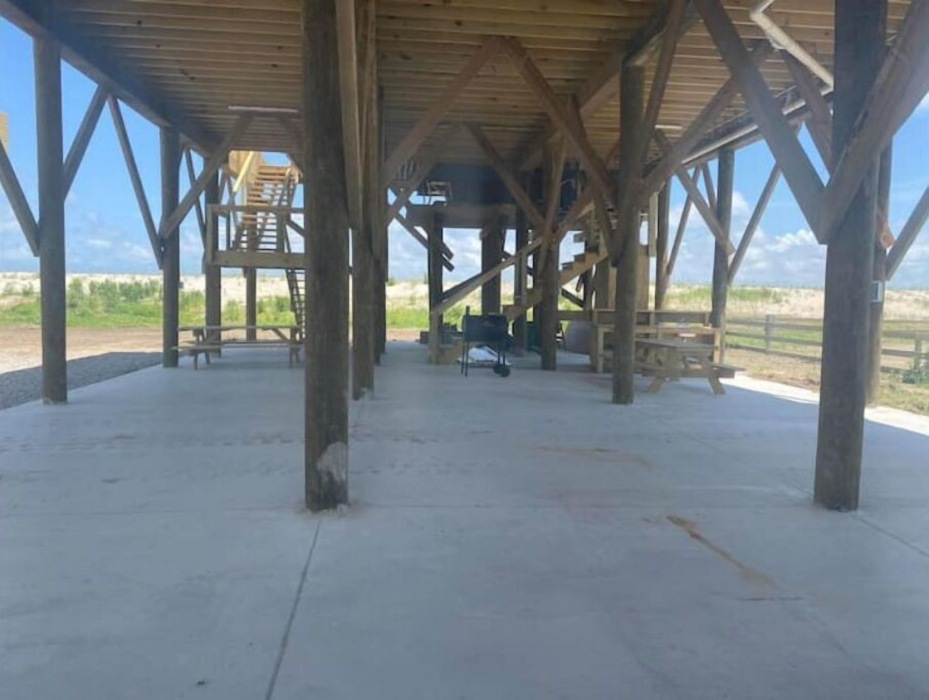 Une structure à ciel ouvert dotée d’un toit en bois et d’un sol en béton, comprenant un escalier et des bancs.