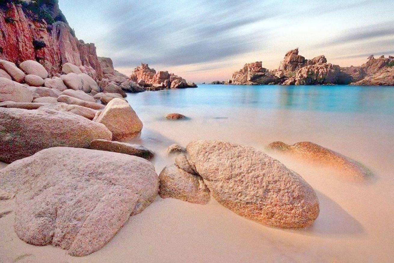Una spiaggia con grosse rocce e acqua calma.