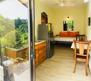 A compact kitchen with a refrigerator, wooden cabinets, and a dining area with a table and chair. - Enchanted Laziness (Manuel Antonio)