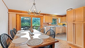 A wooden dining table with chairs, a chandelier, and a view of the outdoors through large windows.