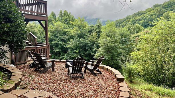 An outdoor seating area with Adirondack chairs and a fire pit, surrounded by a stone border and a wooden deck.