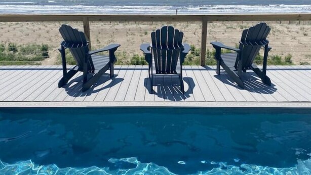 A poolside area with three Adirondack chairs facing a beach view.