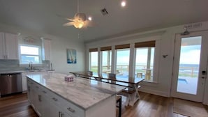 A spacious kitchen with a large island, a dining area with a view, and a door labeled "Beach House".