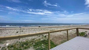 A beach view from a wooden deck with a railing, overlooking the ocean and sandy beach.