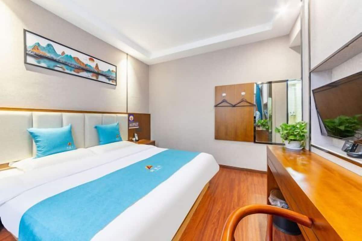 Ein Hotelzimmer mit einem Bett, einem Schreibtisch, einem Sessel, einem Spiegel und einem Bild an der Wand.