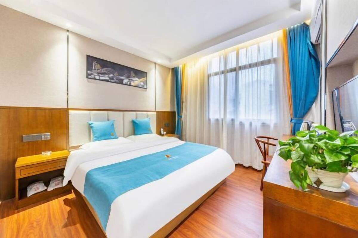 Ein Hotelzimmer mit einem großen Bett, einem Nachttisch, einem Fernseher, einem Fenster mit Vorhängen und einem Bild an der Wand.