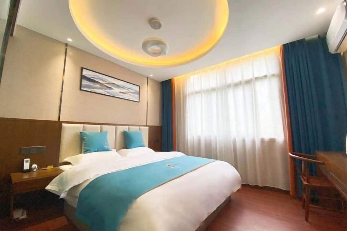 Ein Hotelzimmer mit Bett, Schreibtisch, Stuhl, einem Bild an der Wand und einem Fenster mit Vorhängen.