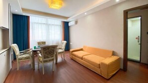 A room with a wooden floor, a yellow sofa, a dining table with chairs, and a television on the wall. - Afuer Chain Smart Hotel (Weixin Lianyi Branch) (Weixin)