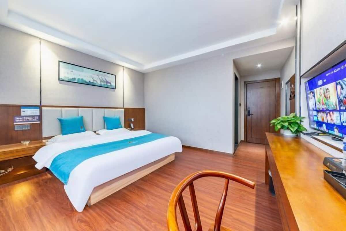 Ein Hotelzimmer mit einem großen Bett, einem Holztisch, einem Fernseher und einem gerahmten Bild an der Wand.