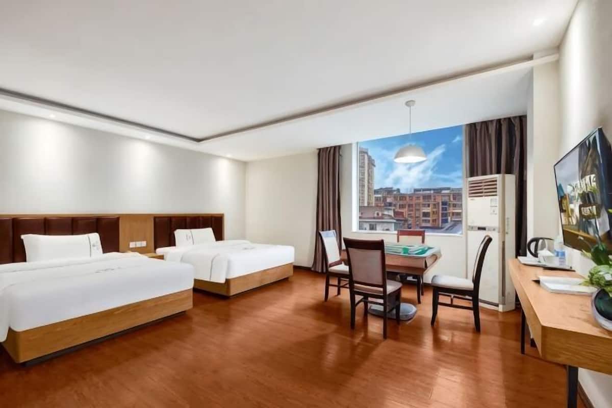Ein Hotelzimmer mit zwei Betten, einem Schreibtisch, einem Stuhl und einem großen Fenster mit Blick auf die Stadt.