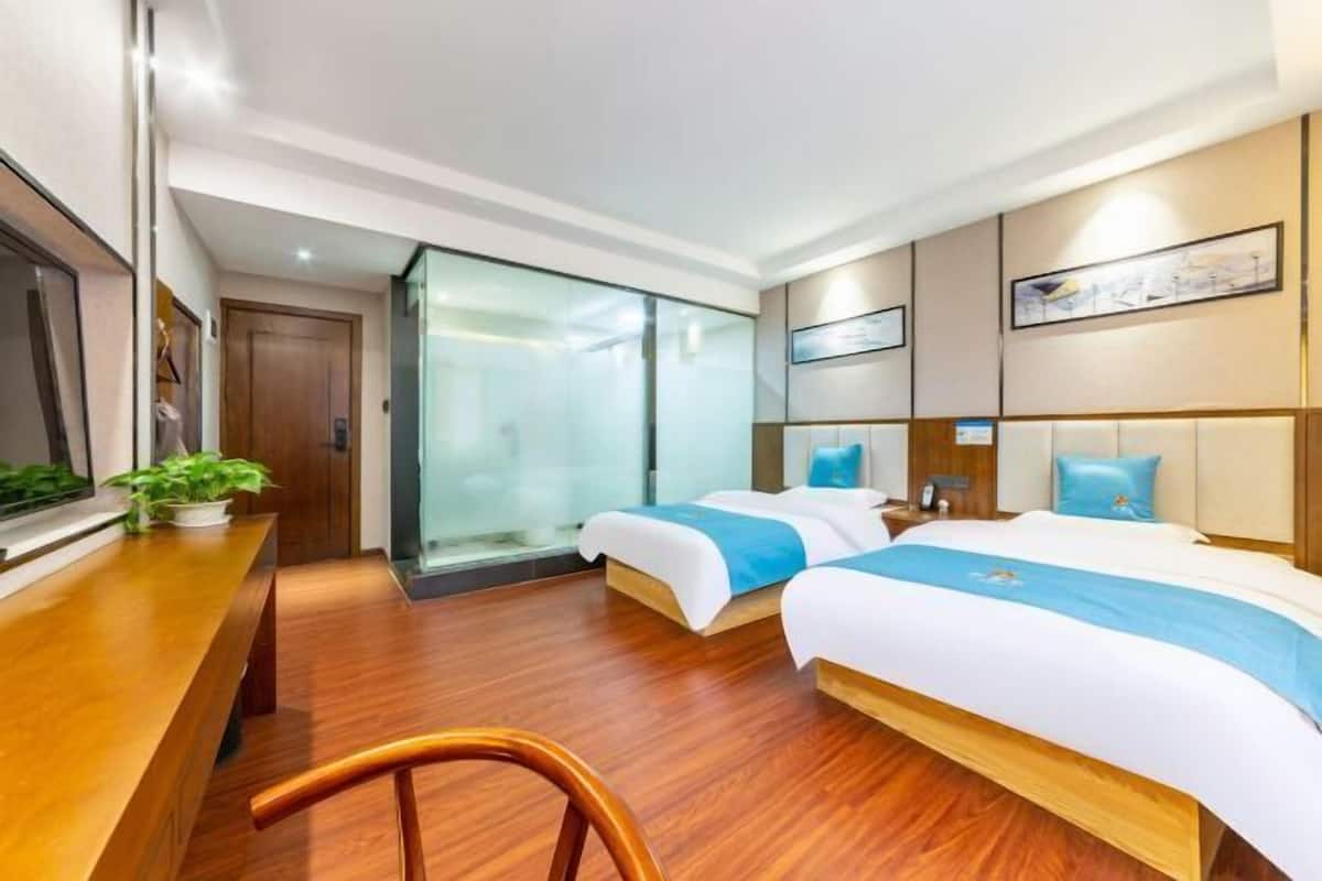 Ein Hotelzimmer mit zwei Betten, einem Holztisch, einem Stuhl, einer Glastür und einem Bild an der Wand.